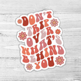 Don't Trip Over What's Behind You Die Cut Sticker, colorful motivational quote sticker with flower illustrations on a wooden background.