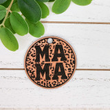 Leopard Mama Leather Keychain, round leather keychain with a leopard print design and 'MA MA' text in black, placed on a white wooden surface with green leaves nearby.