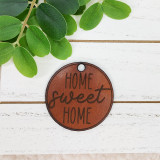 Home Sweet Home Leather Keychain, round brown leather keychain with engraved text 'Home Sweet Home' on white wooden background with green leaves.