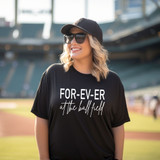 For-Ev-Er At The Ball Field WHITE DTF Heat Transfer, a woman wearing a black t-shirt with white text and sunglasses at a baseball stadium.