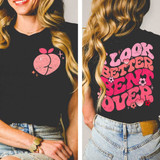 I Look Better Bent Over Distressed DTF Heat Transfer, image of a woman wearing a black t-shirt with a pink distressed graphic of a peach with leaves on the front and back with the text "I Look Better Bent Over" in bold pink letters.