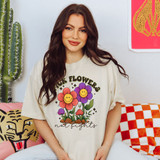 Pick Flowers Not Fights DTF Heat Transfer, colorful graphic t-shirt with smiling cartoon flowers and the text 'Pick Flowers Not Fights' worn by a woman with brown hair.