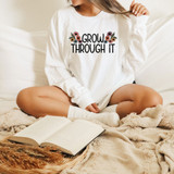 Grow Through It DTF Heat Transfer, a colorful floral design with motivational text on a white long-sleeve shirt worn by a person sitting on a bed.