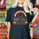 Band Tee NV DTF Heat Transfer, Coral-colored design featuring Nirvana band logo, smiley face with crossed-out eyes, and band details from Aberdeen, Washington, on a black t-shirt worn by a woman with blonde hair.