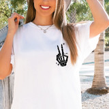 Skellie Hand Peace Sign DTF Heat Transfer, black skeleton hand making a peace sign with sparkly stars around it on a white t-shirt worn by a smiling woman outdoors.