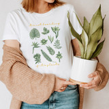 It's Not Hoarding If It's Plants DTF Heat Transfer, woman wearing a white T-shirt with green plant graphics and orange text, holding a potted plant.