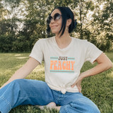 Just Peachy Retro DTF Heat Transfer, a woman sitting outdoors on grass wearing a T-shirt with retro 'Just Peachy' design in peach and black colors.