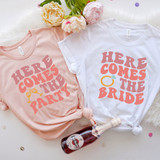 Here Comes The Bride DTF Heat Transfer, white T-shirt with wedding ring graphic and text, and pink T-shirt with party glasses graphic and text.