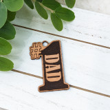 Dad Leather Keychain, a customized wooden keychain featuring the word 'DAD' with a hashtag symbol, placed on a white wooden surface beside green leaves, ideal for Father's Day gift.
