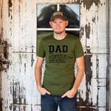 Dad Definition DTF Heat Transfer, a man wearing a green t-shirt with the word "DAD" and a definition printed on it, standing in front of a rustic wooden background.