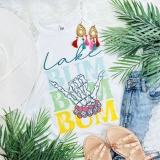 Lake Bum Stacked Screen Print Heat Transfer, colorful graphic t-shirt with skeleton hand making a peace sign, surrounded by tropical leaves, denim shorts, a white hat, and beige sandals.