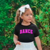 Dance DTF Heat Transfer, pink text design on a black t-shirt worn by a young girl with a white bow in her hair outdoors.