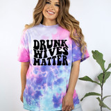 Drunk Wives Matter DTF Heat Transfer, a woman wearing a colorful tie-dye t-shirt with the bold black text "Drunk Wives Matter" printed on the front.