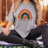 Fall Is My Favorite Rainbow DTF Heat Transfer, a woman wearing a light grey t-shirt with a colorful rainbow, a pumpkin, and autumn leaves graphic and the text 'Fall Is My Favorite' printed on it.