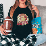 Spartans Mascot DTF Heat Transfer, close-up of a woman wearing a black T-shirt with the Spartans mascot logo, holding an American football, sitting on a couch with snacks nearby.