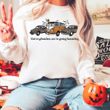 Get In Goulies DTF Heat Transfer, Halloween-themed design on white sweatshirt featuring haunted cars and pumpkin with the text 'Get in ghoules, we're going haunting'.