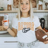 Gators, vibrant custom color options DTF Heat Transfer on a woman's athletic white t-shirt with orange and black Gators logo and text, holding a football.