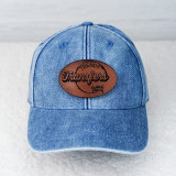 Custom Leather Hat Patch, a brown leather patch with black embroidered text and design, attached to a blue denim baseball cap.