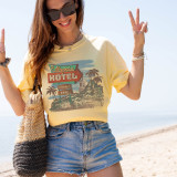 Hotel California Screen Print Heat Transfer, woman wearing a yellow t-shirt with a vintage hotel and palm trees design, standing on a beach.