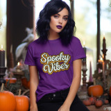 Spooky Vibes Sequins and Chenille Patch, a colorful patch with the words "Spooky Vibes" in cursive, embellished with sequins and chenille embroidery on a purple T-shirt worn by a woman in a Halloween-themed setting.