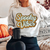 Spooky Vibes Sequins and Chenille Patch, close-up of a woman wearing a light gray sweatshirt with "Spooky Vibes" embroidered in white, black, and orange sequins, holding a black mug in her right hand.