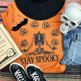 Stay Spooky Black PUFF Screen Print Heat Transfer, Halloween-themed t-shirt with skeleton and jack-o'-lantern graphics, surrounded by Halloween accessories.