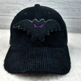 Mini Bat Chenille Patch, black velvety bat-shaped patch with purple embroidered eyes on a black corduroy hat