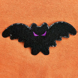 Mini Bat Chenille Patch, black bat shaped embroidered patch with purple eyes on orange fabric background.