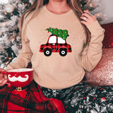 Plaid Car with Christmas Tree DTF Heat Transfer, Christmas-themed graphic on a beige sweatshirt worn by a person sitting near a decorated Christmas tree.
