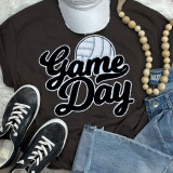 Volleyball Black Game Day Chenille Patch, close-up view of a black t-shirt with a volleyball graphic and 'Game Day' text, accompanied by a baseball cap, sneakers, denim jeans, and a wooden bead necklace.