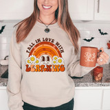 Fall In Love With Learning DTF Heat Transfer, a woman wearing a sweatshirt with a colorful fall-themed design including a rainbow, daisies, and autumn leaves, holding a matching mug with the same phrase.