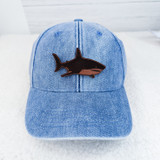 Shark Leather Hat Patch, a black and brown embroidered patch of a shark sewn onto a light blue denim baseball cap.