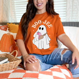 Boo-Jee WHITE DTF Heat Transfer, image of a woman wearing a Halloween-themed t-shirt with a ghost holding a pink drink, decorated for fall with pumpkins in the background.