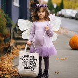 Call Me Cute And Give Me Candy DTF Heat Transfer, a young girl dressed as a fairy with white wings, holding a pink star-shaped lollipop and a tote bag with Halloween-themed design on a fall street scene.
