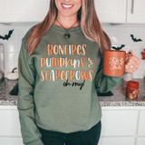 Bonfires Pumpkins Scarecrows Oh My! DTF Heat Transfer, a woman wearing a holiday-themed sweatshirt in a kitchen, holding a fall-themed mug, with Halloween decorations in the background.