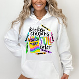 Broken Crayons Still Color DTF Heat Transfer, colorful graphic design on a white hoodie with crayons and the phrase "Broken crayons still color."