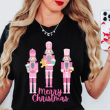 Merry Christmas Pink Nutcrackers DTF Heat Transfer, pink nutcracker characters with Christmas treats and the text Merry Christmas in pink on a black T-shirt.