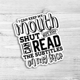 I Can Keep My Mouth Shut Die Cut Sticker, humorous black and white sticker with text design saying 'I can keep my mouth shut but you can read the subtitles on my face' on a light wooden background.