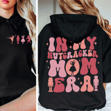 In My Nutcracker Mom Era DTF Heat Transfer, a design featuring silhouettes of ballet dancers, nutcracker figures, and a girl with a nutcracker on her head, in pink and peach colors on black hoodies.