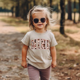 Mini Cowhide Pink DTF Heat Transfer, a pink and black leopard print design on a children's T-shirt, worn by a smiling girl with sunglasses outdoors.