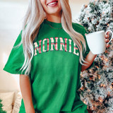 Nonnie Plaid DTF Heat Transfer, close-up on a person wearing a green t-shirt with the word 'NONNIE' in holiday plaid design, holding a white mug, with a Christmas tree in the background.