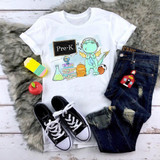 Back To School Dragon Blue Pre-K Sublimation Transfer, image of a white t-shirt with a cartoon dragon wearing headphones and surrounded by school-related items.