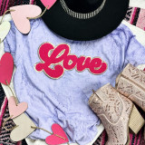 Hot Pink Love Chenille Patch, pink and gold embroidered patch with the word 'Love' on a purple marble-textured t-shirt surrounded by pink and white heart-shaped decorations, beige cut-out sandals with intricate cut-out design and a chunky heel.