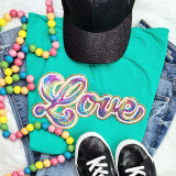 RAINBOW LOVE Sequin Patch, colorful embroidered patch spelling 'Love' with rainbow-colored sequins on a teal T-shirt.