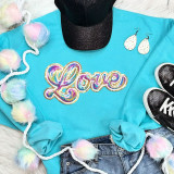 RAINBOW LOVE Sequin Patch, colorful rainbow love embroidery on turquoise sweatshirt with fluffy pom-pom trim, paired with black sneakers and white polka dot earrings.