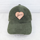 Lover Leather Hat Patch, green corduroy baseball cap with a pink heart-shaped patch embroidered with the word "Lover" in black cursive font.