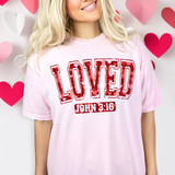 Loved John 3:17 Hearts DTF Heat Transfer, a pink t-shirt with a love-themed design and biblical verse print, surrounded by paper hearts.