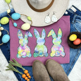 Three Rainbow Bunnies Screen Print Heat Transfer, colorful pastel bunny designs on pink T-shirt surrounded by Easter decorations.