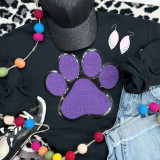 Dog Paw Purple Chenille Patch, purple and black embroidered fabric patch in the shape of a dog paw print with sequins on a black clothing item.