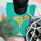 Margarita Glass Sequin Patch, colorful summer fashion accessories display with a turquoise T-shirt, black cap, pearl necklace, denim shorts, black sneakers, and tropical plant leaves.